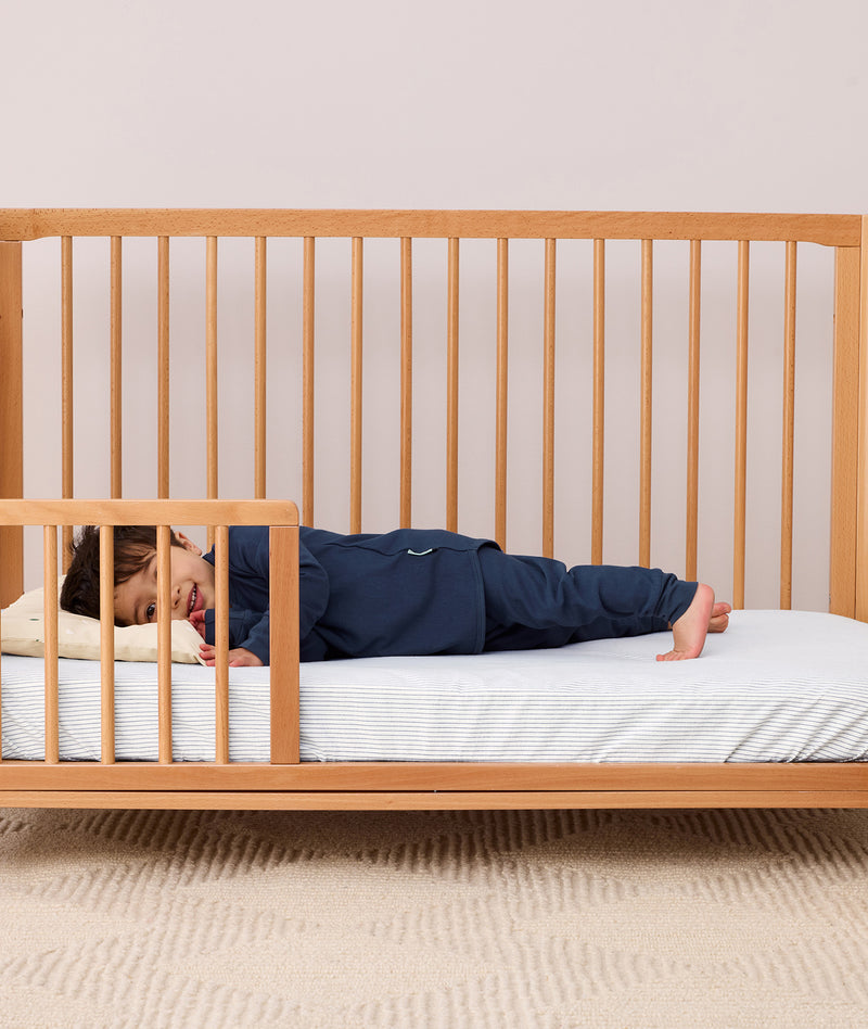Toddler lying on their side in a crib wearing a navy blue long-sleeve pyjama set with matching pants, featuring a relaxed fit.