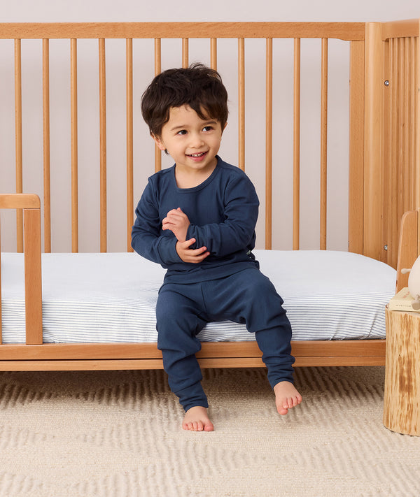 Toddler sitting on a bed wearing a navy blue Long Sleeve Pyjamas with matching pants, featuring a soft breathable fabric.