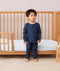 Toddler standing in front a crib wearing a navy blue long-sleeve pyjama set with matching pants, made from soft organic cotton and bamboo.