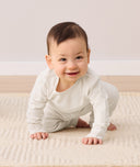 A smiling baby crawls toward the camera, wearing a two-piece ergoPouch baby pyjama set.