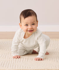 A smiling baby crawls toward the camera, wearing a two-piece ergoPouch baby pyjama set.