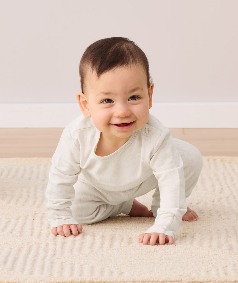 A smiling baby crawls toward the camera, wearing a two-piece ergoPouch baby pyjama set.