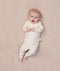 A baby lying on a soft beige surface, wearing a long-sleeve, cream-colored pyjama set with a snug fit and a shoulder snap.