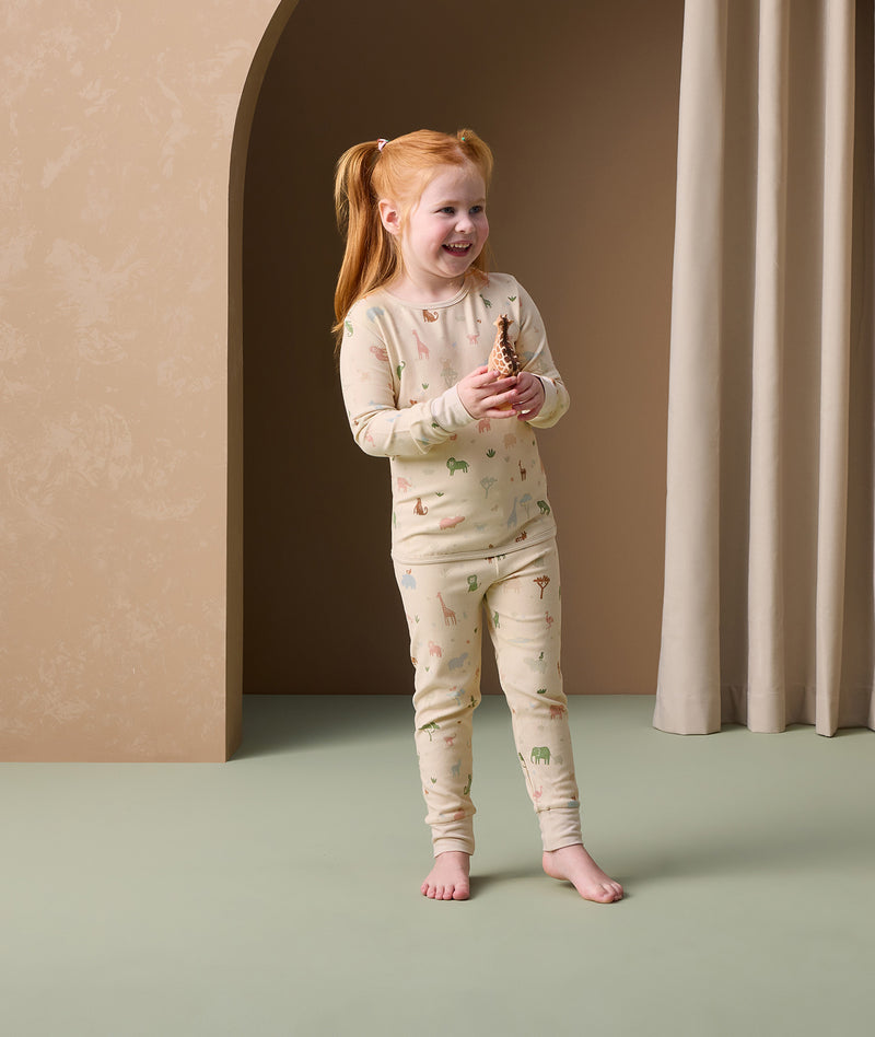 A preschooler is smiling while wearing snug-fitting, safari-themed long sleeve pyjamas from ergoPouch.