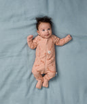 Baby lying on a soft blue sheet, wearing an ergoPouch Long Sleeve Layer in Elephant Parade