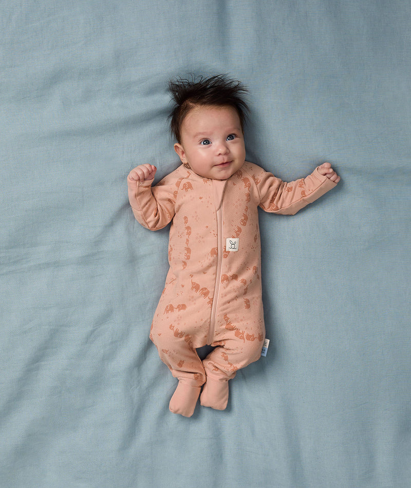 Baby lying on a soft blue sheet, wearing an ergoPouch Long Sleeve Layer in Elephant Parade