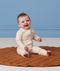 Smiling baby sitting on a brown mat, wearing a cream patterned Long Sleeve Layer 0.2 TOG