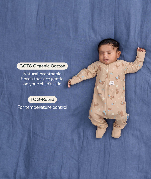 Sleeping baby in a tan patterned Long Sleeve Layer on a blue background, featuring text highlighting GOTS Organic Cotton and TOG-Rated features.