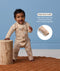 Baby wearing a patterned tan Long Sleeve Layer leaning against a wooden stool featuring text highlighting fold-over cuffs.