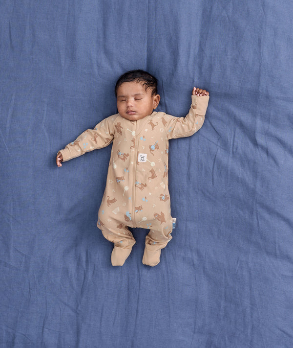 Sleeping baby lying on a blue blanket wearing a beige patterned Long-Sleeve Layer with fold-over foot cuffs.