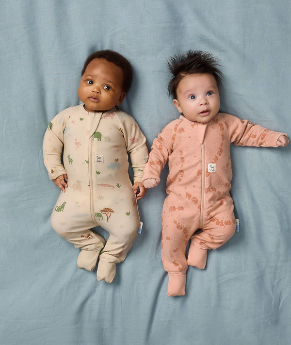 Two babies lying side by side wearing ergoPouch Long Sleeve Layer in Savannah and Elephant Parade.