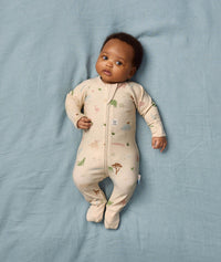 Baby is lying on a soft blue sheet, wearing an ergoPouch Long Sleeve Layer that features a safari animal print and fold-over foot cuffs.