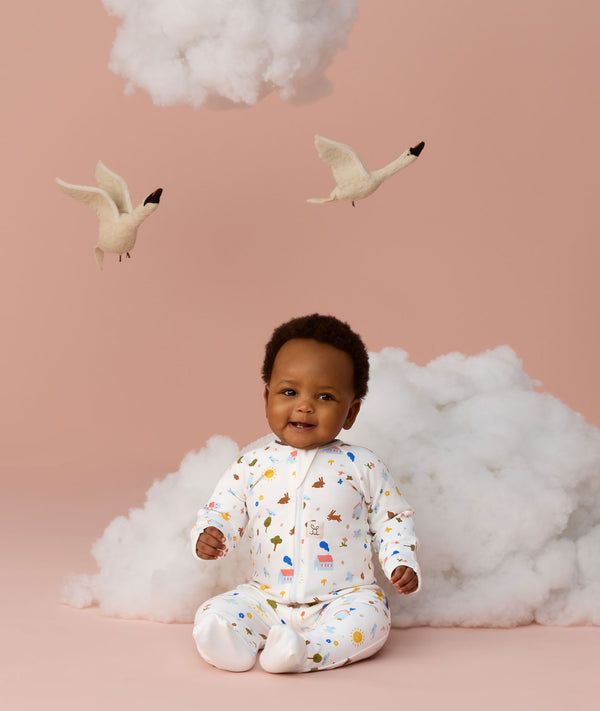 Baby wearing a white slim-fit Long Sleeve Layer sitting upright against a light pink background with decorative birds and clouds.
