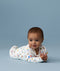 Infant lying on its stomach against a blue background wearing a white Long Sleeve Layer with colourful all-over print.
