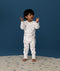 Toddler standing on a rug against a deep blue background wearing a white Long Sleeve Layer, featuring a front zipper and colourful all-over print.