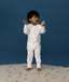 Toddler standing on a rug against a deep blue background wearing a white Long Sleeve Layer, featuring a front zipper and colourful all-over print.