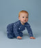Baby crawling on a light blue background wearing a blue Long Sleeve Layer with an all-over moon-and-star print, looking slightly to the side.
