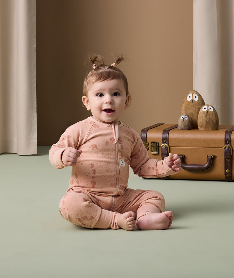 An infant sits cozily in an ergoPouch Long Sleeve Layer, featuring an elephant print and a snug fit.