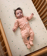 Baby is lying in a cot, wearing an ergoPouch Long Sleeve Layer with its foot cuffs folded over for extra warmth and protection.