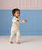 Toddler walking indoors wearing an off-white, subtly patterned Long Sleeve Layer against a blue wall background.