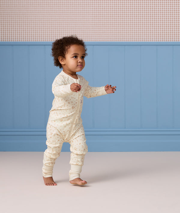 Toddler walking indoors wearing an off-white, subtly patterned Long Sleeve Layer against a blue wall background.