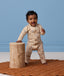 Baby wearing a patterned tan Long-Sleeve Layer leaning against a wooden stool.