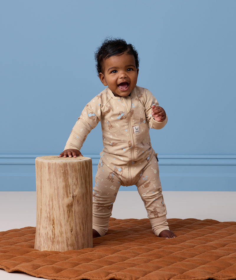 Baby wearing a patterned tan Long-Sleeve Layer leaning against a wooden stool.
