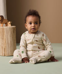 Infant sitting on the floor in ergoPouch Long Sleeve Layer Savannah with foot cuffs folded over.