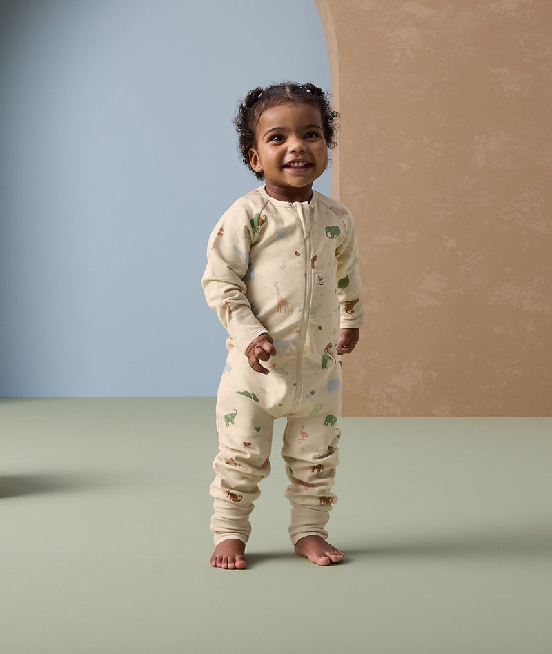 Smiling toddler in ergoPouch Long Sleeve Layer Savannah, featuring a front zipper and safari animal print.