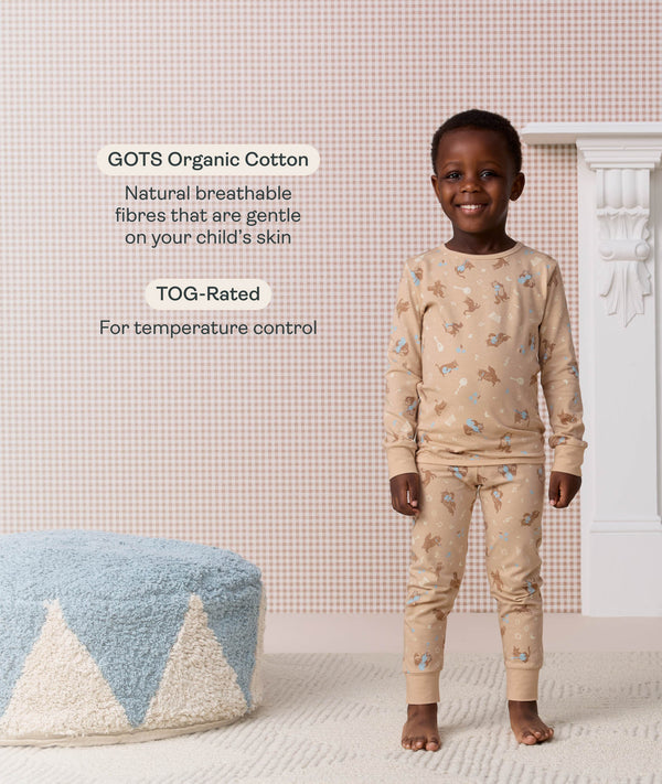 Preschooler standing and smiling in a beige patterned Long Seeve Pyjama set with product feature callout highlighting GOTS organic cotton and TOG rating