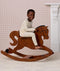 Preschooler wearing a cream patterned Long Sleeve Pyjamas, riding a wooden rocking horse.