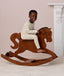 Preschooler wearing a cream patterned Long Sleeve Pyjamas, riding a wooden rocking horse.