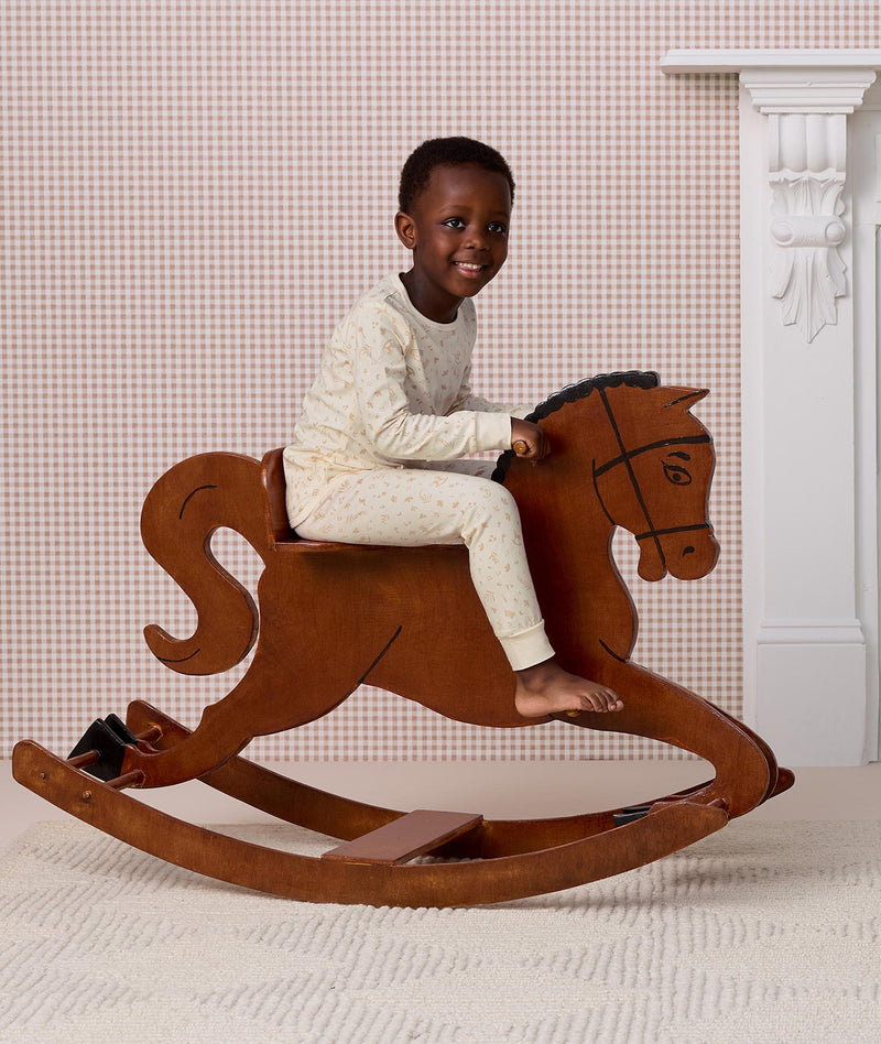 Preschooler wearing a cream patterned Long Sleeve Pyjamas, riding a wooden rocking horse.
