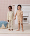 Two preschoolers holding hands, wearing ergoPouch Pyjama Sets. The young boy is wearing a cream Long Sleeve Pyjama Set, while the girl is wearing a tan Short Sleeve Pyjama Set.