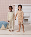 Two preschoolers holding hands, wearing ergoPouch Pyjama Sets. The young boy is wearing a cream Long Sleeve Pyjama Set, while the girl is wearing a tan Short Sleeve Pyjama Set.