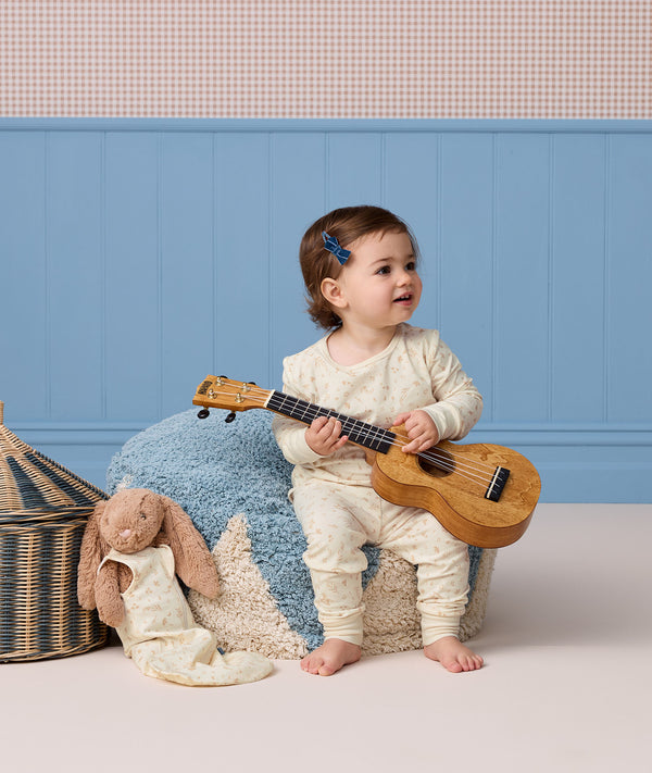 Toddler sitting on a blue textured pouf playing a ukulele while wearing cream-colored Long Sleeve Pyjamas with a subtle pattern.