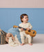 Toddler sitting on a blue textured pouf playing a ukulele while wearing cream-colored Long Sleeve Pyjamas with a subtle pattern.