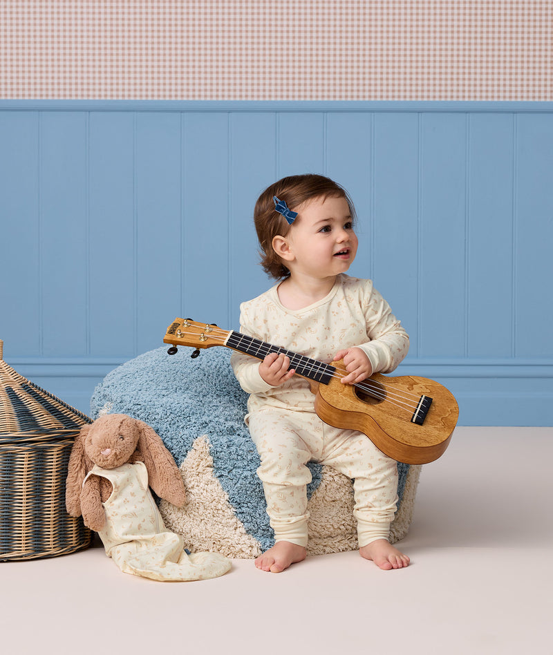 Toddler sitting on a blue textured pouf playing a ukulele while wearing cream-colored Long Sleeve Pyjamas with a subtle pattern.