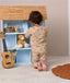 Child wearing a beige patterned Long Sleeve Pyjamas kneeling in front of a wooden dollhouse.