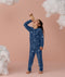 Preschooler wearing blue Long Sleeve Pyjamas with a moon-and-star print, standing barefoot against a soft pink background and looking upward while holding a toy telescope, surrounded by fluffy cloud props.