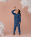 Preschooler wearing blue Long Sleeve Pyjamas with a moon-and-star print, standing barefoot against a soft pink background and looking upward while holding a toy telescope, surrounded by fluffy cloud props.