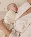 Sleeping baby wrapped in a cream-colored Cocoon Swaddle Bag, resting in mum's arms.