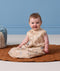 Baby sitting on a brown quilted mat wearing a beige pattern-printed Sleeping Bag made from premium cotton.