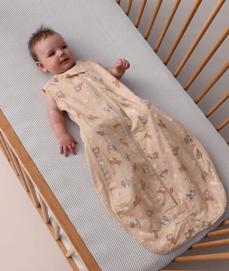 Baby lying in a wooden cot wearing a sleeveless, patterned Premium Sleeping Bag 1.0 TOG made from soft, breathable materials for ultimate comfort.