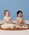 Two babies sitting side by side wearing ergoPouch Premium Sleeping Bag 1.0 TOG in Lullaby and Melody.