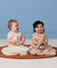 Two babies sitting side by side wearing ergoPouch Premium Sleeping Bag 1.0 TOG in Lullaby and Melody.
