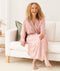 Woman sits on the edge of a sofa, laughing, wearing ergoPouch Matchy Matchy bamboo robe in Daisies