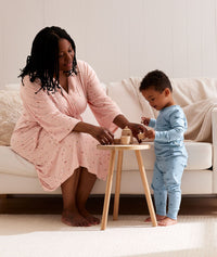 Mum wearing the ergoPouch Matchy Matchy bamboo maternity robe in Daisies plays with wooden tea set with toddler 