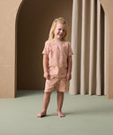 A preschooler stands smiling, wearing short-sleeve ergoPouch pyjamas made from organic cotton that is gentle on the skin.