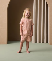A preschooler stands smiling, wearing short-sleeve ergoPouch pyjamas made from organic cotton that is gentle on the skin.